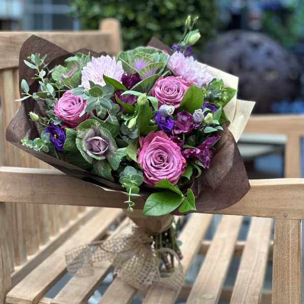 Bouquet of pink roses and purple flowers wrapped in brown paper