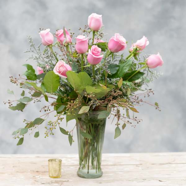 Pink roses arranged in a clear glass vase with greenery