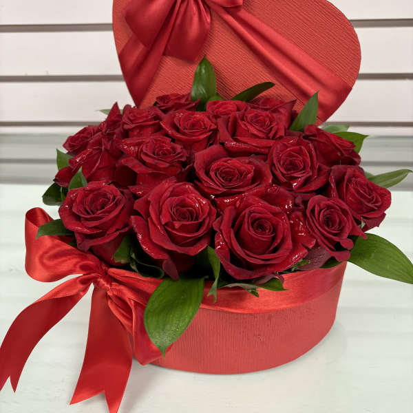 Red roses arranged in a heart-shaped box with a satin bow