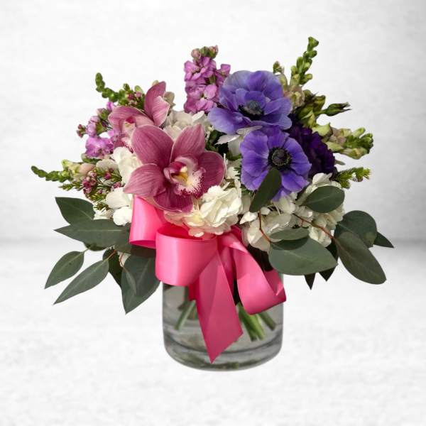 Pink and purple flowers arranged in a glass vase with a bright pink ribbon