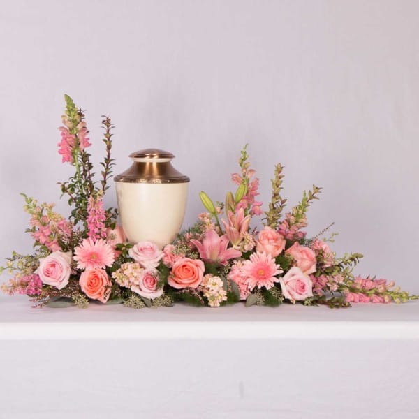 Pink floral arrangement surrounding a gold urn