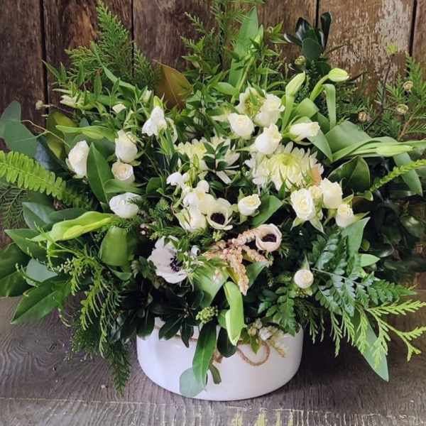 White floral arrangement in a round white box with lush greenery