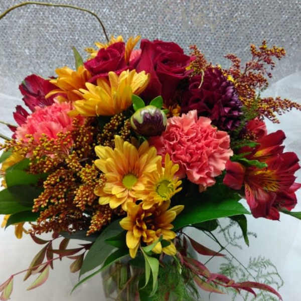 Mixed bouquet of red roses, yellow daisies, and pink carnations in a glass vase