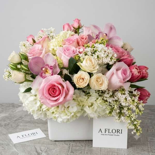 Pink and white floral arrangement in a white square container