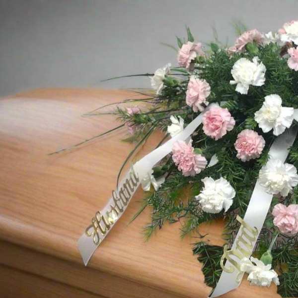 Pink and white floral spray on a casket with ribbon streamers
