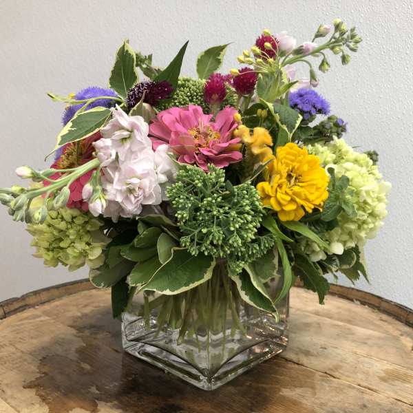 Mixed bouquet in a square glass vase with pink, yellow, purple, and green blooms