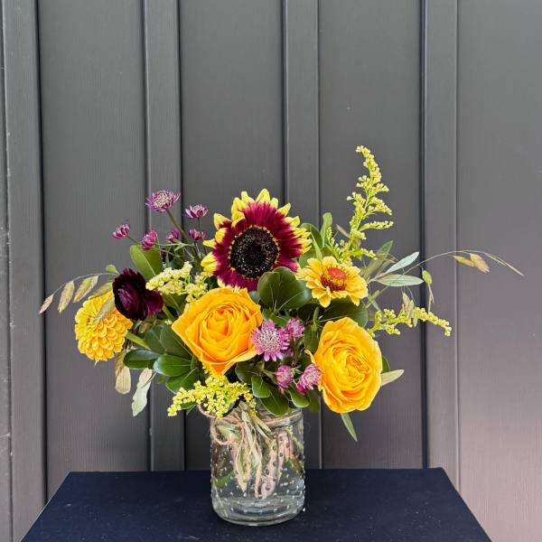 Bouquet of yellow and burgundy flowers in a clear glass jar