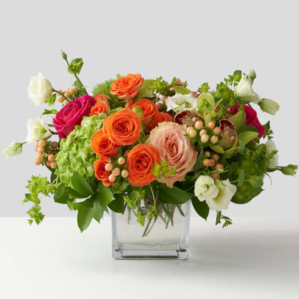Mixed bouquet of orange, pink, and white roses in a clear glass vase