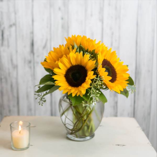Sunflower bouquet in a glass vase beside a lit candle