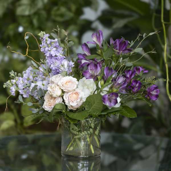 Purple and blush flowers arranged in a clear glass vase
