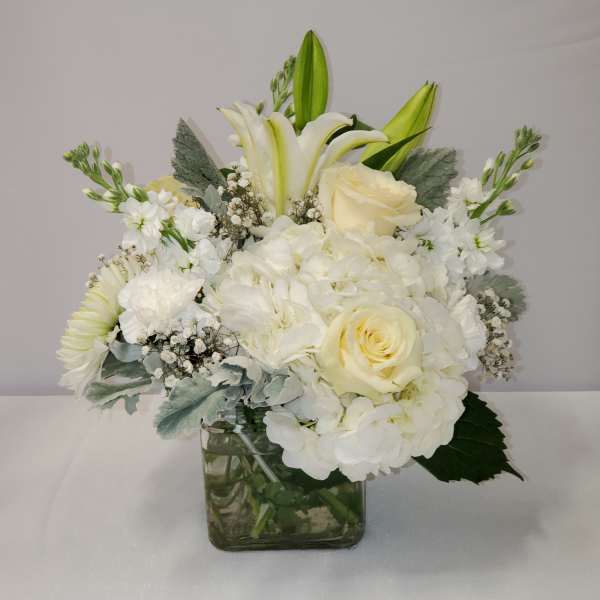 Compact white and ivory bouquet of roses, lilies, and hydrangeas in a clear glass cube vase