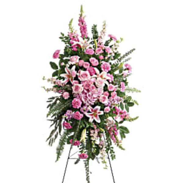 Tall standing spray of pink and white roses, lilies, and carnations on a metal easel.