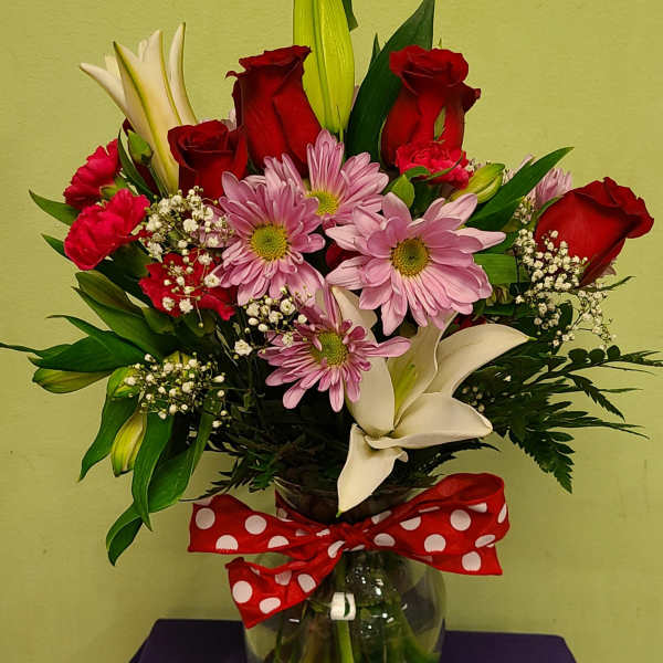 Bouquet of red roses, pink daisies, and white lilies in a glass vase