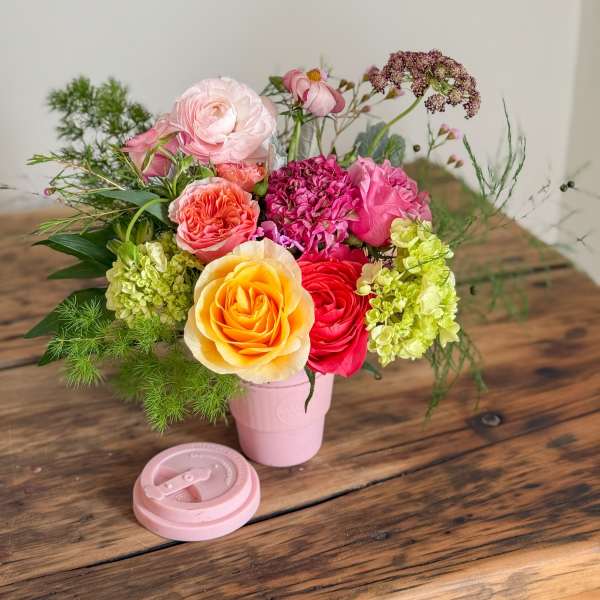 Mixed bouquet of roses and hydrangeas in a pink cup-style vase