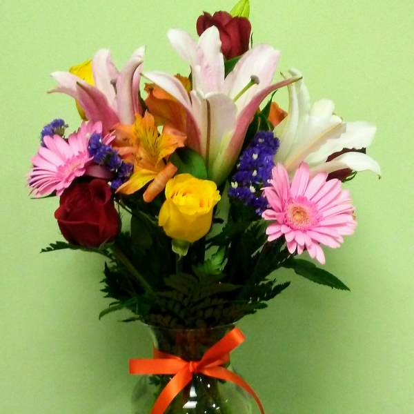 Mixed bouquet of lilies, roses, and daisies in a glass vase with a ribbon