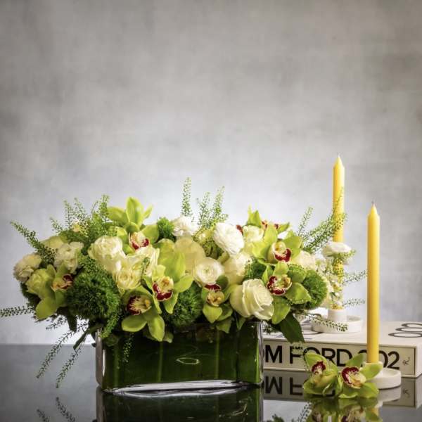 Green and white floral arrangement in a glass vase with yellow candles