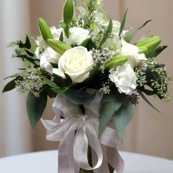 White roses and lilies arranged in a glass vase with a silver ribbon