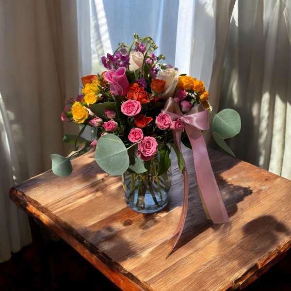 Mixed roses in a glass vase with a pink ribbon