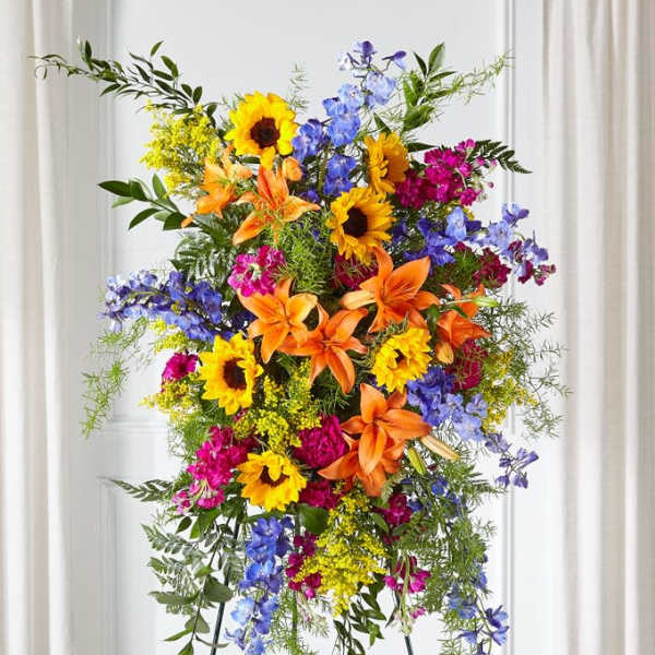 Tall standing floral spray with sunflowers, lilies, and blue flowers