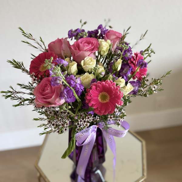 Pink roses and purple flowers in a purple vase with a ribbon