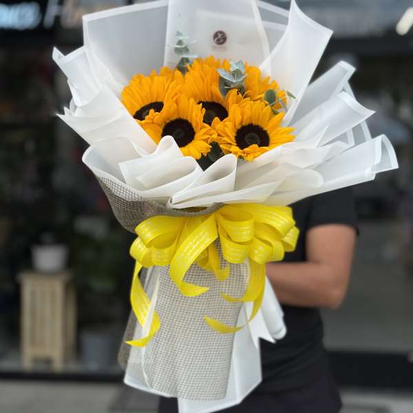 Bouquet of bright yellow sunflowers wrapped in white paper with a yellow ribbon
