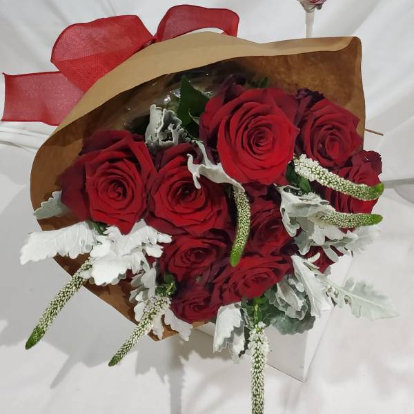 Bouquet of red roses with white filler flowers wrapped in brown paper and red ribbon