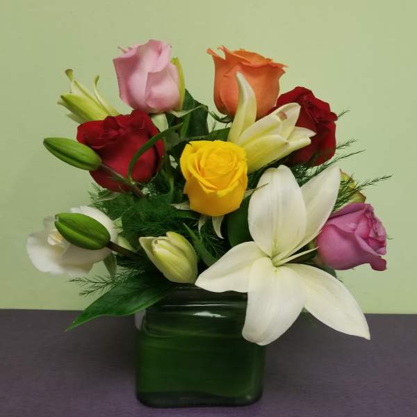 Mixed roses and lilies arranged in a green glass vase