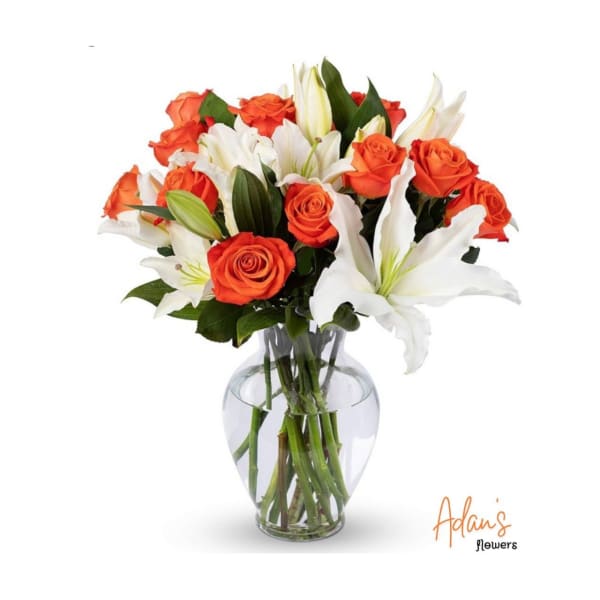Orange roses and white lilies arranged in a clear glass vase