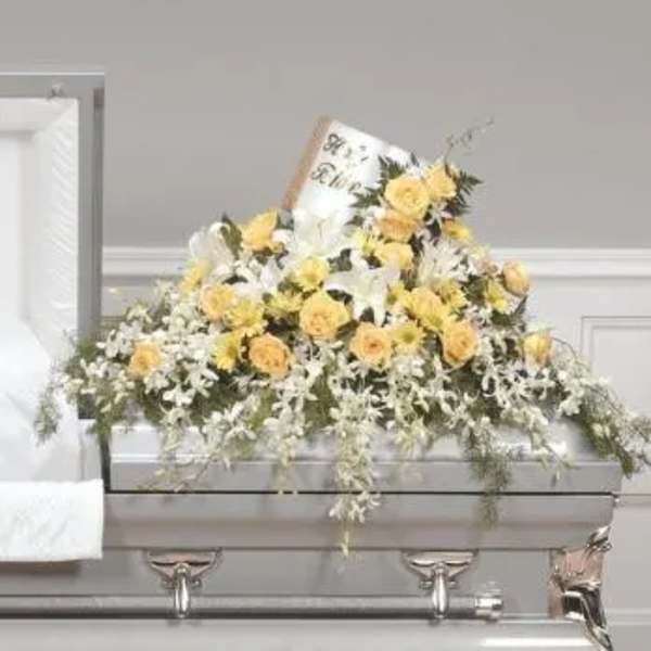 Yellow and white floral casket spray on a gray casket