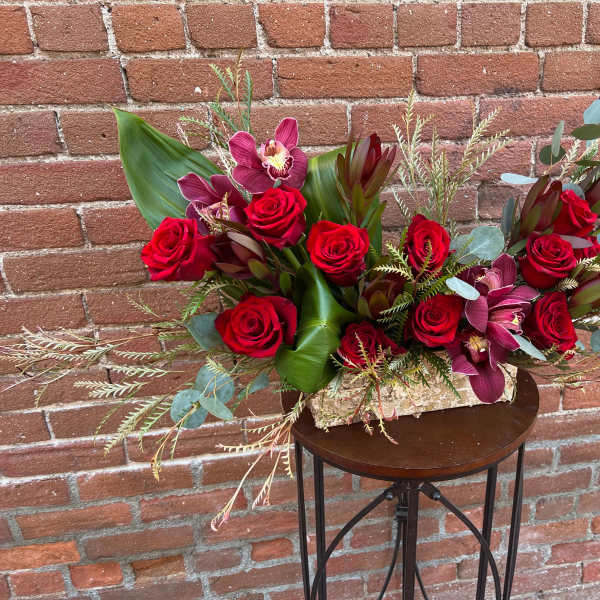 Red roses and burgundy orchids in a low rectangular arrangement