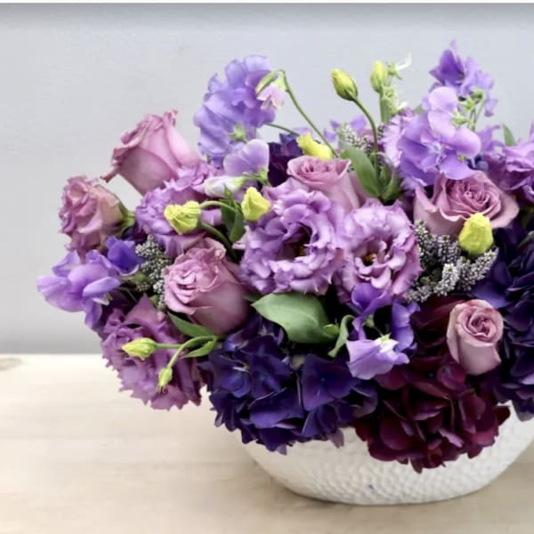 Purple and pink floral arrangement in a white bowl vase
