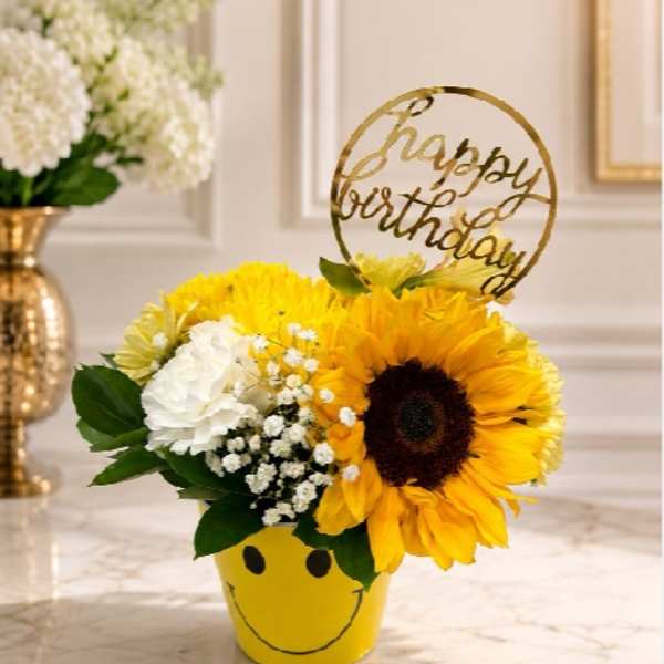 Sunflower and white flower arrangement in a yellow smiley-face pot with a birthday topper