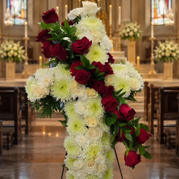 Standing cross covered in white flowers and red roses in a church