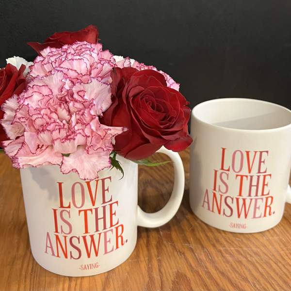 Red roses and pink carnations in a white mug beside a matching mug