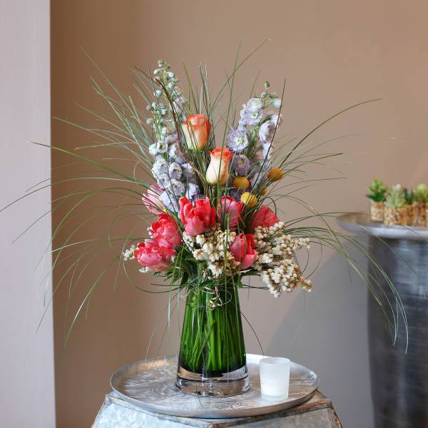 Tall floral arrangement with pink and peach blooms in a glass vase