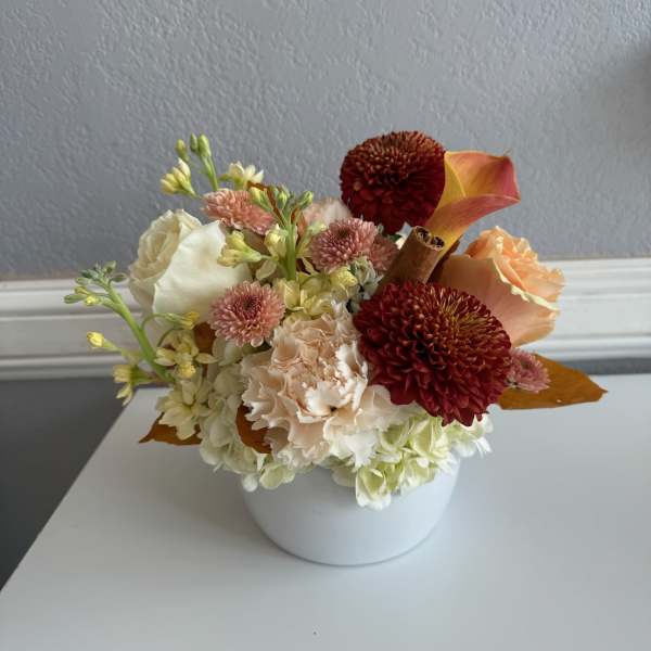 Compact floral arrangement in a white bowl vase with cream, peach, and burgundy blooms