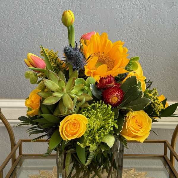 Yellow roses, a sunflower, and succulents arranged in a clear glass vase