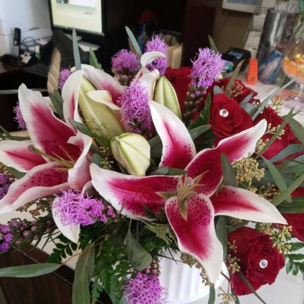 Bouquet of pink-and-white lilies and red roses in a white vase