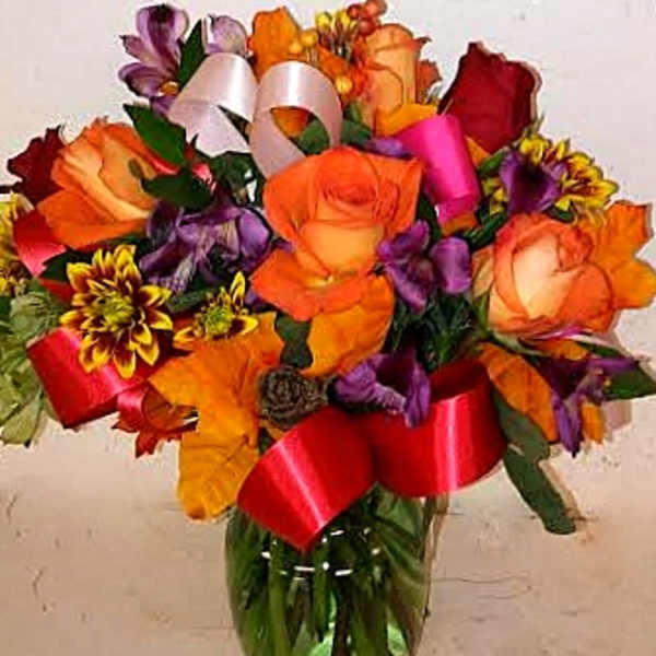 Bouquet of orange, red, and purple flowers in a glass vase with ribbons