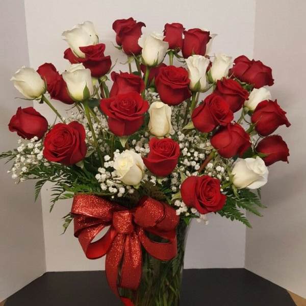 Red and white roses arranged in a glass vase with a red ribbon