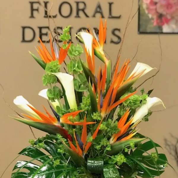 Tropical arrangement with orange bird-of-paradise and white calla lilies in a tall vase