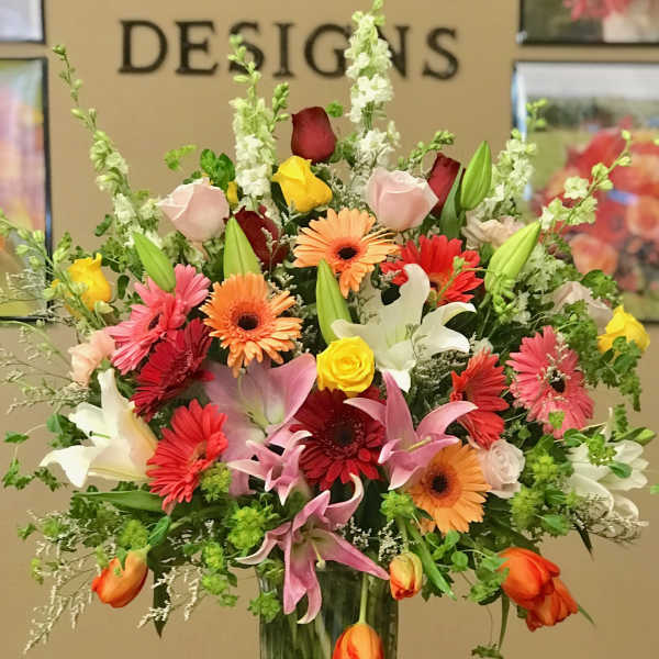 Mixed bouquet of roses, lilies, and gerbera daisies in a tall glass vase