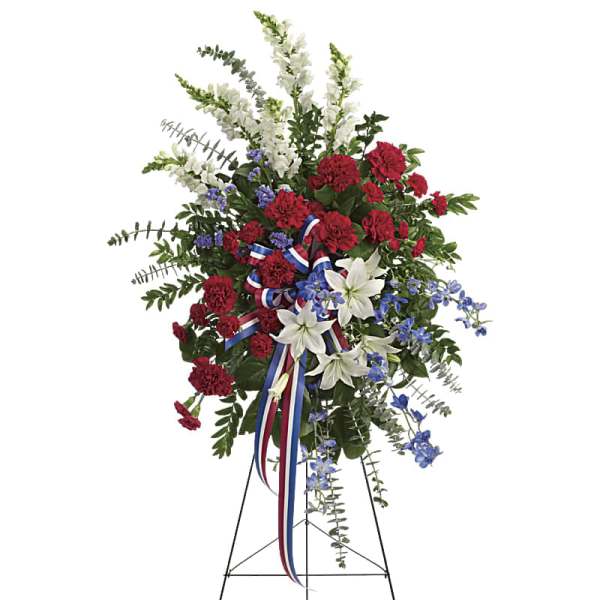 Standing floral spray with red carnations, white lilies, and blue accents