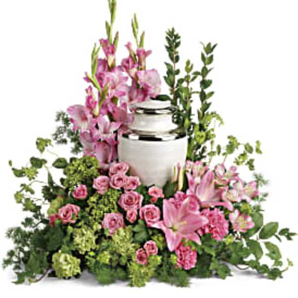 Pink lilies, roses, and carnations arranged around a white cremation urn.