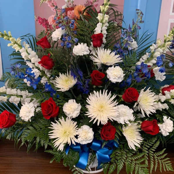 Large red, white, and blue floral arrangement in a basket with a blue ribbon