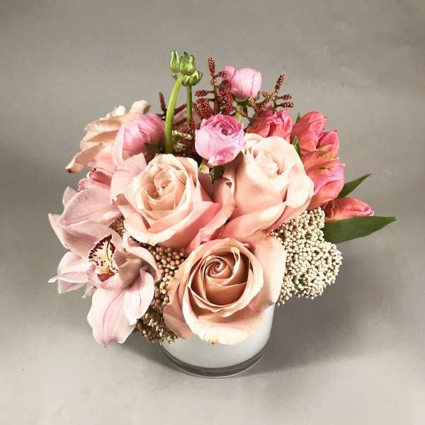 Pink and peach roses with orchids arranged in a white vase