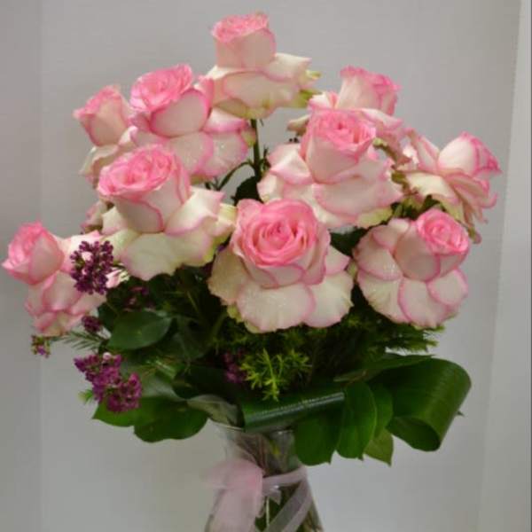 Pink-tipped roses arranged in a clear glass vase with a pink ribbon