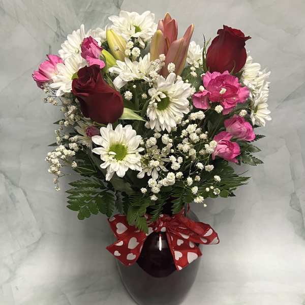 Bouquet of red roses, pink carnations, and white daisies in a dark vase
