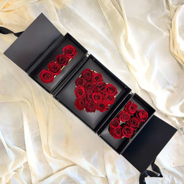 Black gift boxes with red roses arranged inside on cream fabric