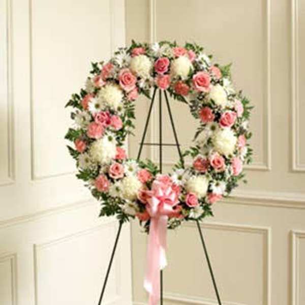 Standing wreath of pink roses and white flowers on an easel with a pink bow
